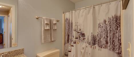 Un baño con inodoro, lavamanos y cortina de ducha con motivo invernal.