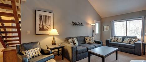 A living room with a staircase, two sofas, a coffee table, and a lamp.