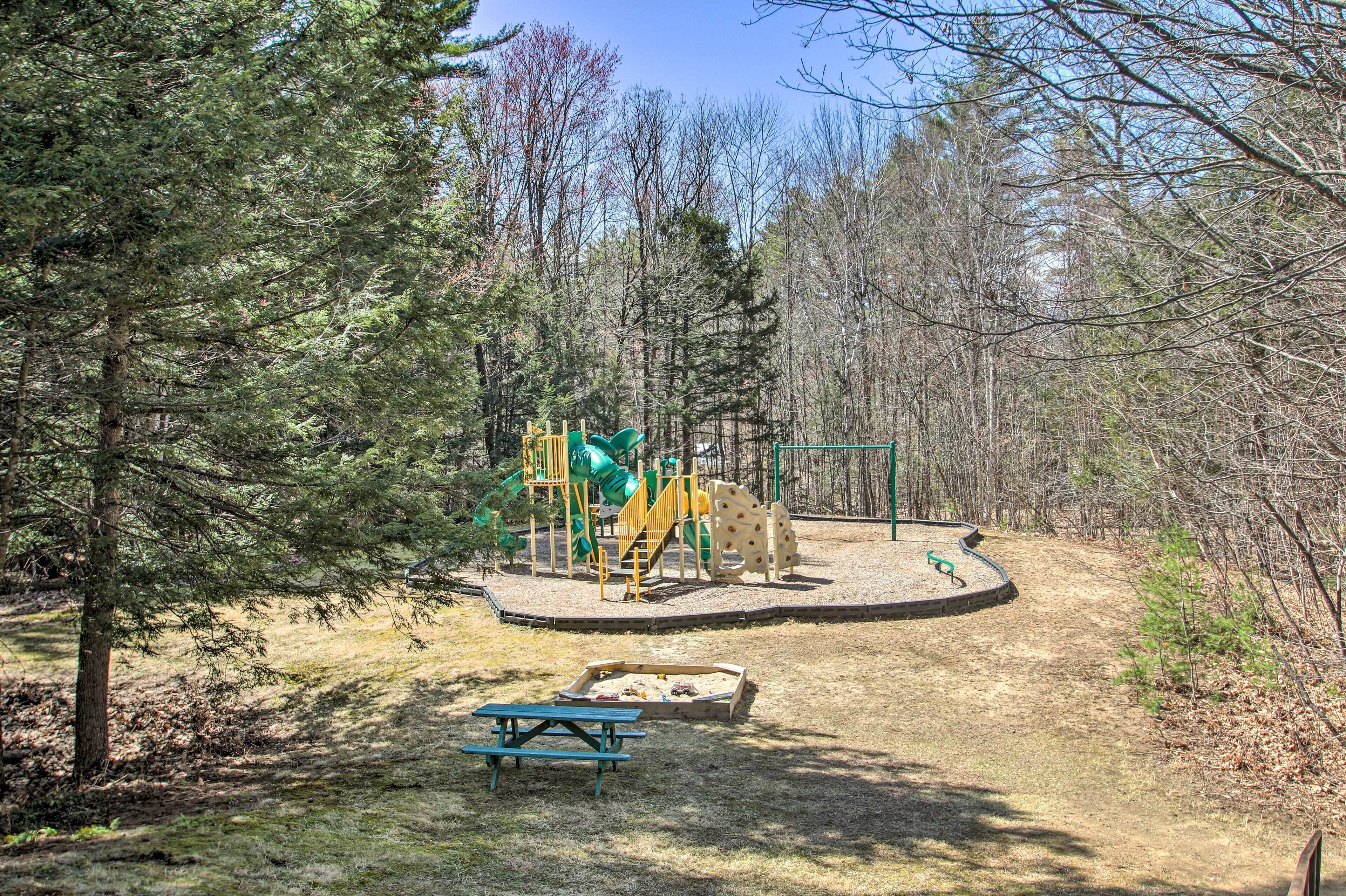 Un parque infantil con tobogán, estructuras para escalar y una mesa de picnic en un área boscosa.