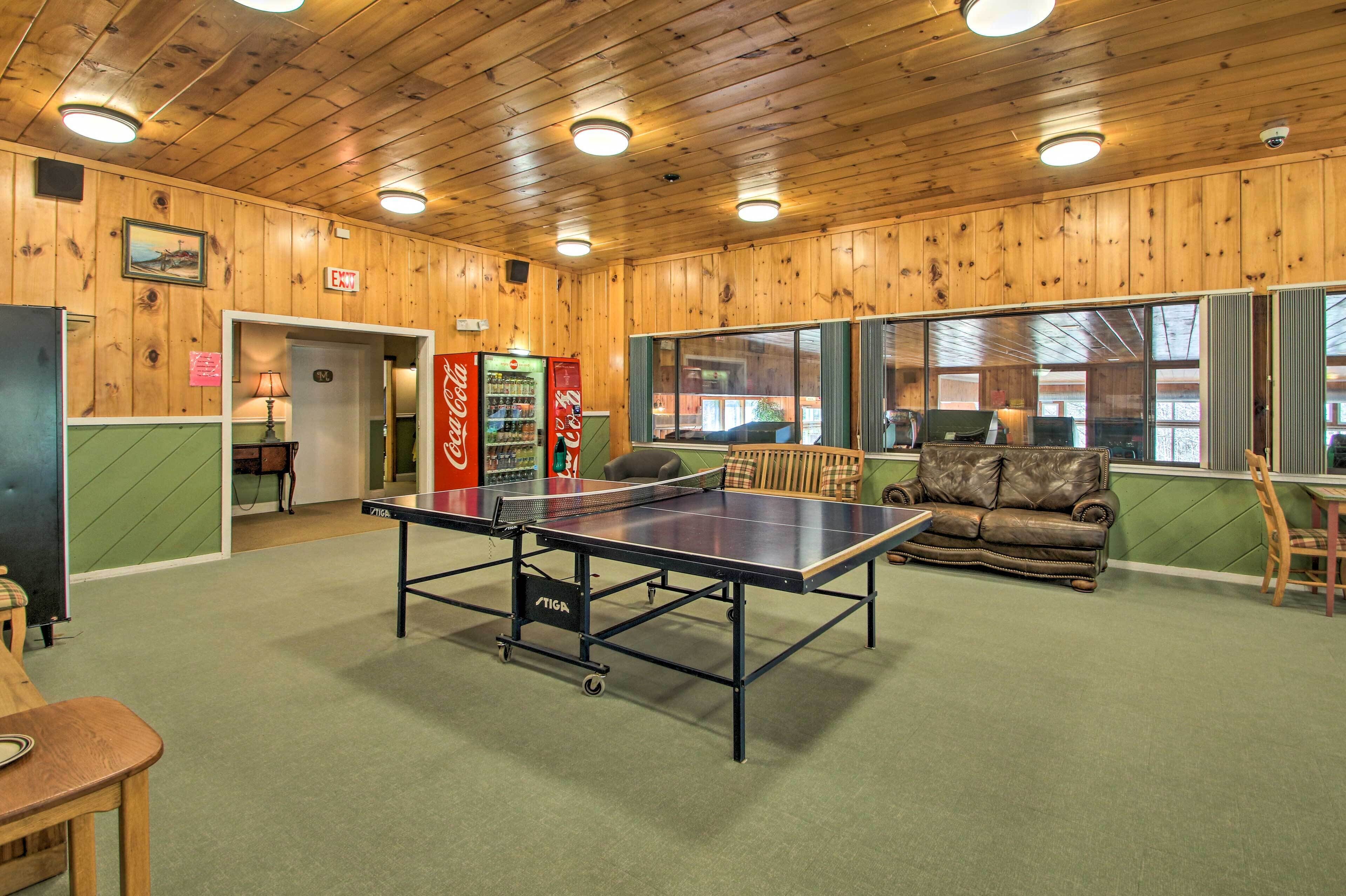 Une pièce avec une table de ping-pong, un canapé, une chaise et un réfrigérateur rempli de Coca-Cola.