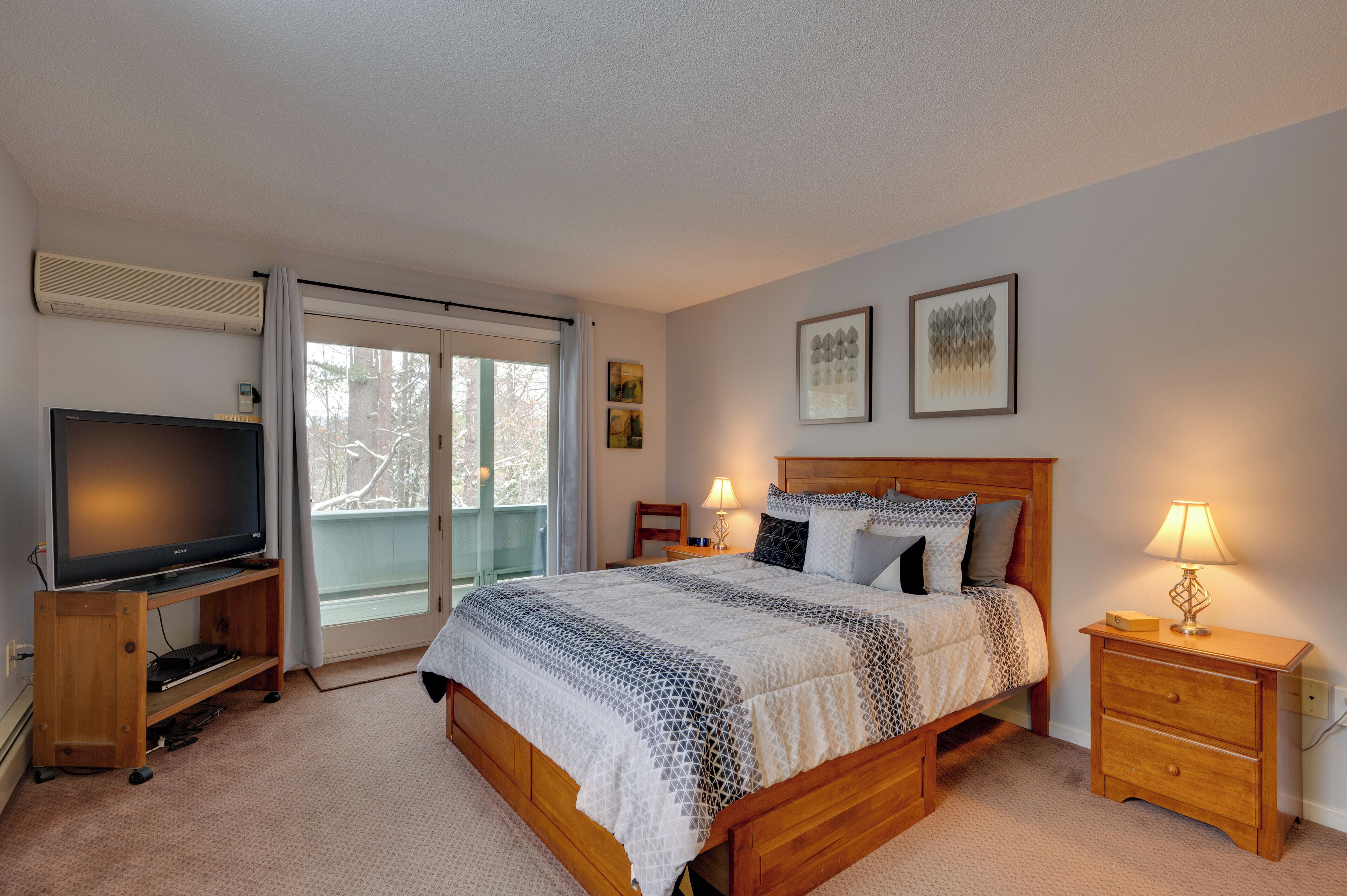A bedroom with a bed, bedside lamps, a TV on a stand, and a sliding glass door to a balcony.