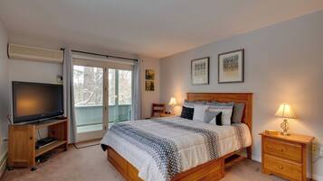 A bedroom with a bed, bedside lamps, a TV on a stand, and a sliding glass door to a balcony.