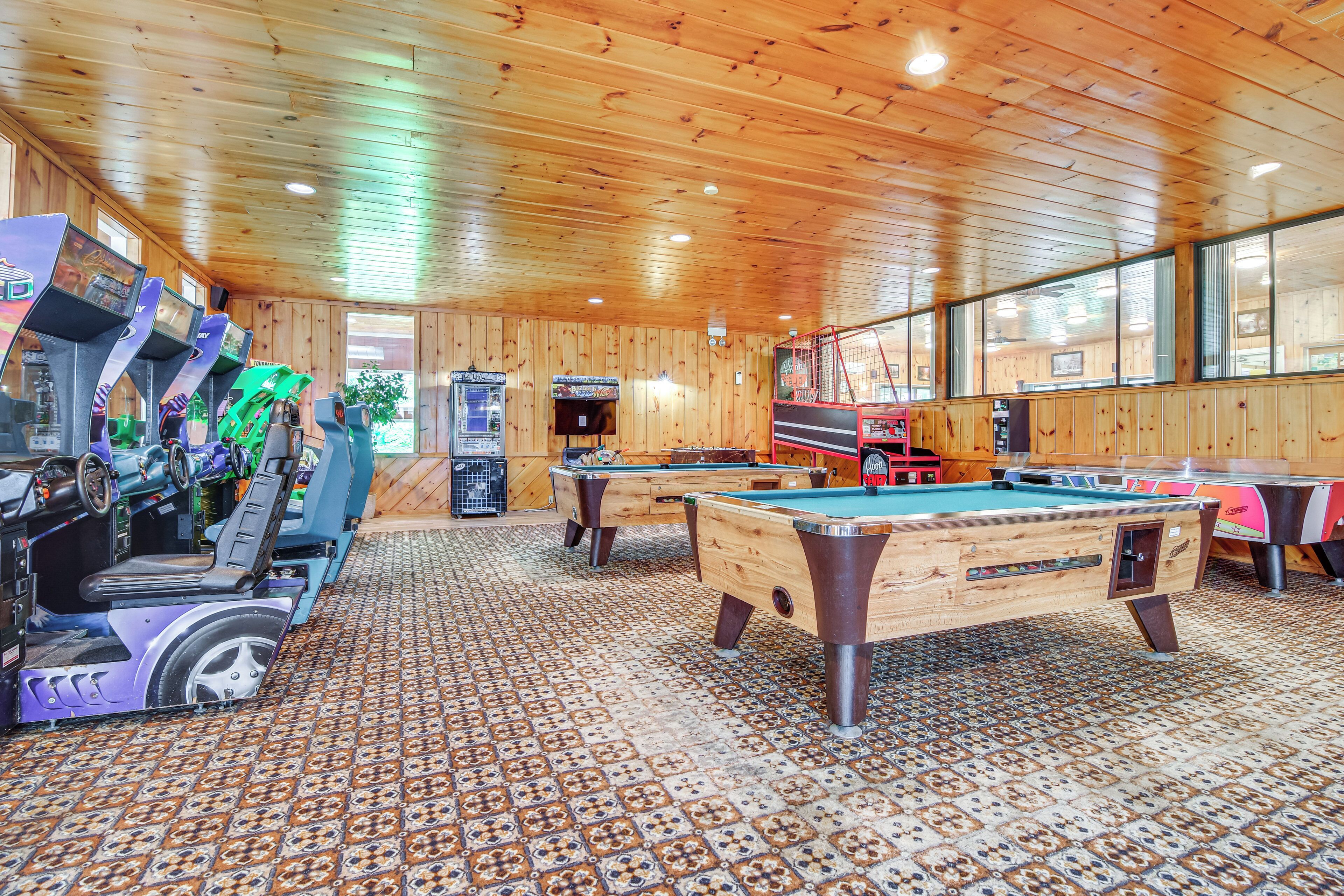 A pool hall with wooden walls and ceiling, multiple pool tables, and a row of arcade machines.