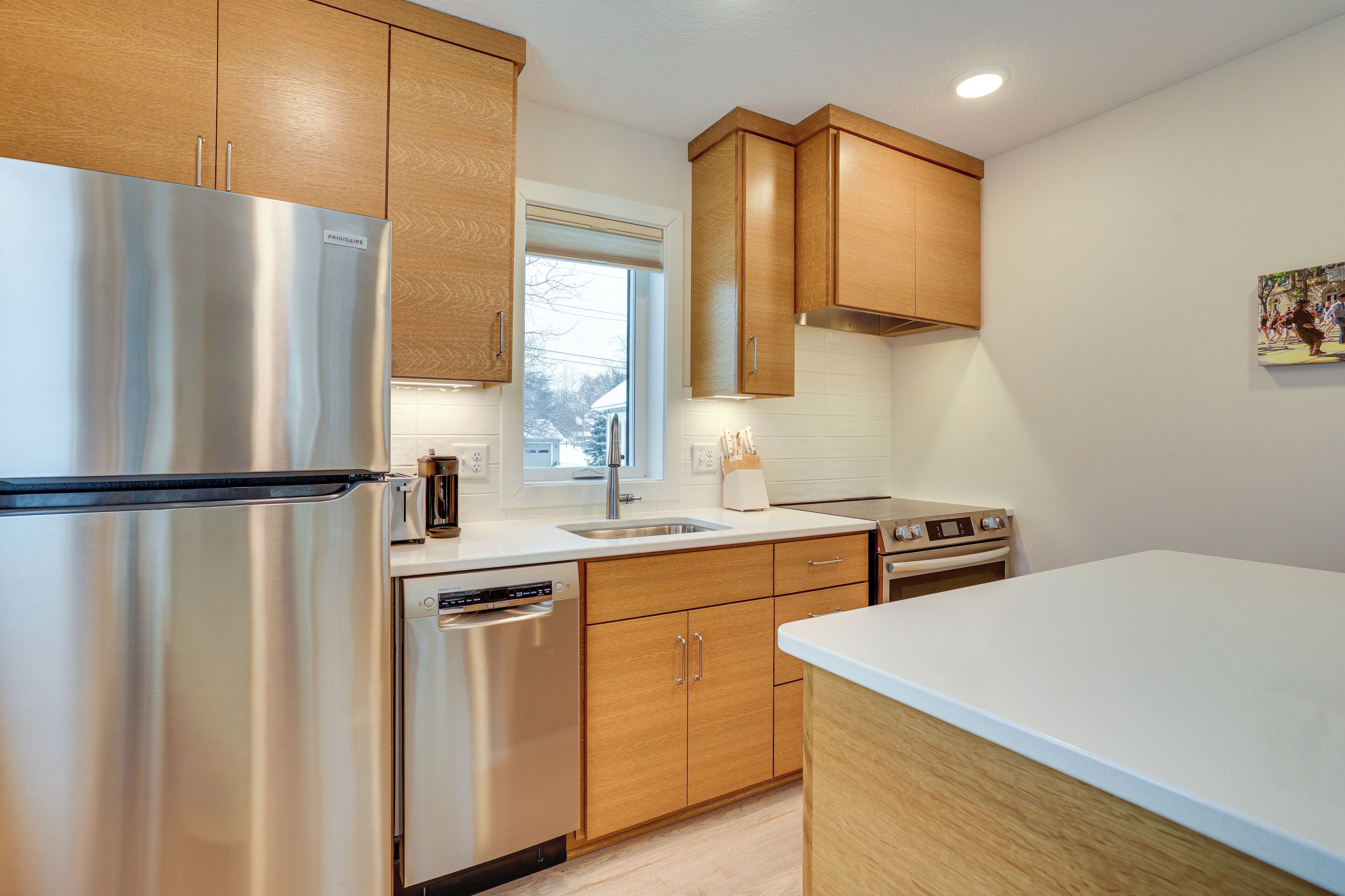A modern kitchen with stainless steel appliances, wooden cabinets, and a white countertop.