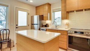Una cocina moderna con armarios de madera, un refrigerador de acero inoxidable, un horno y una encimera blanca.