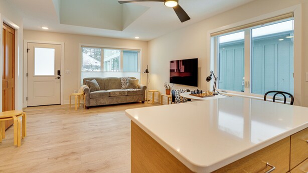 Una cocina moderna con una isla central, un comedor con mesa y sillas, un sofá y un ventilador de techo.