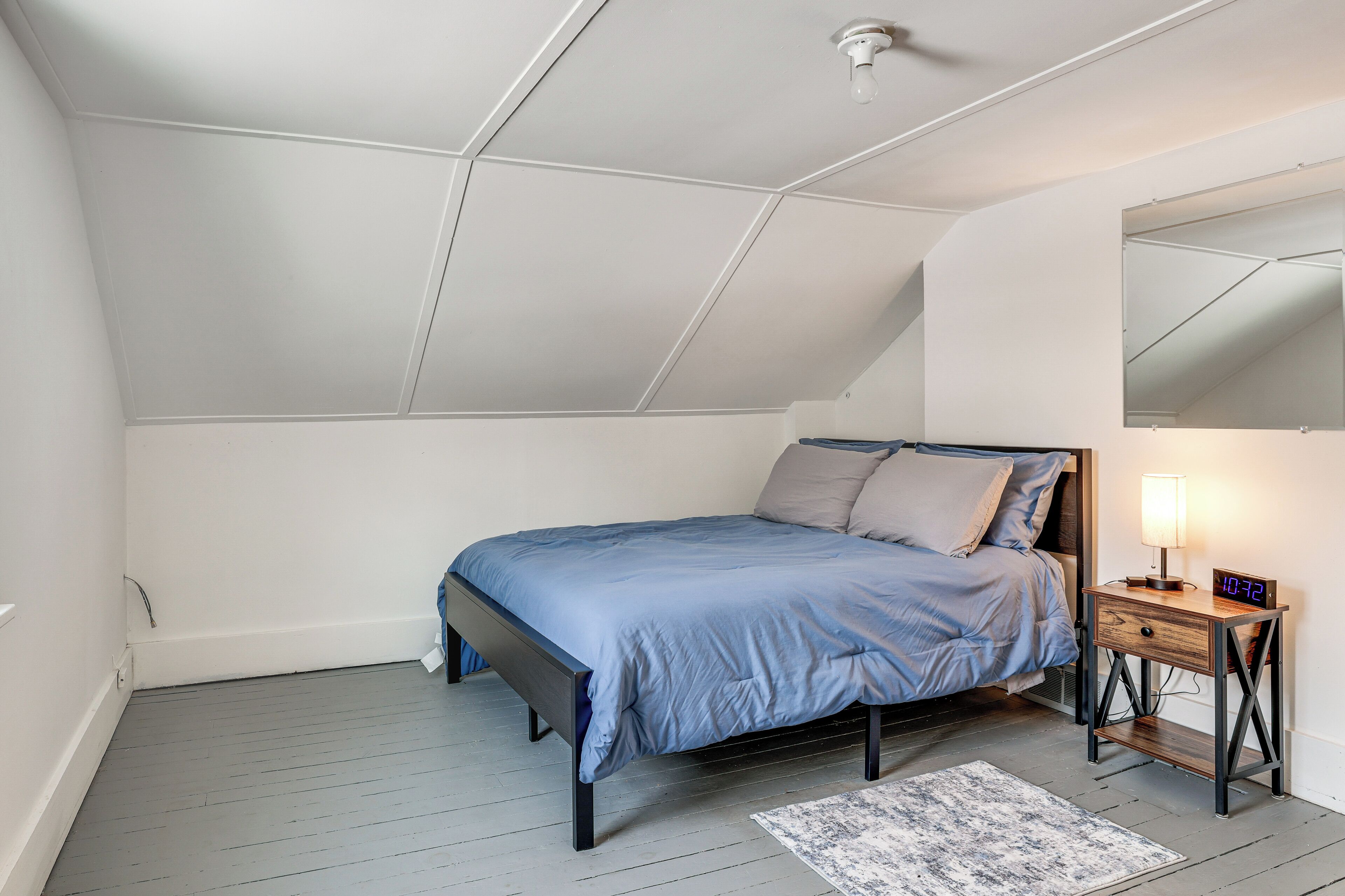 A bedroom with a bed, bedside table, lamp, and a digital clock.