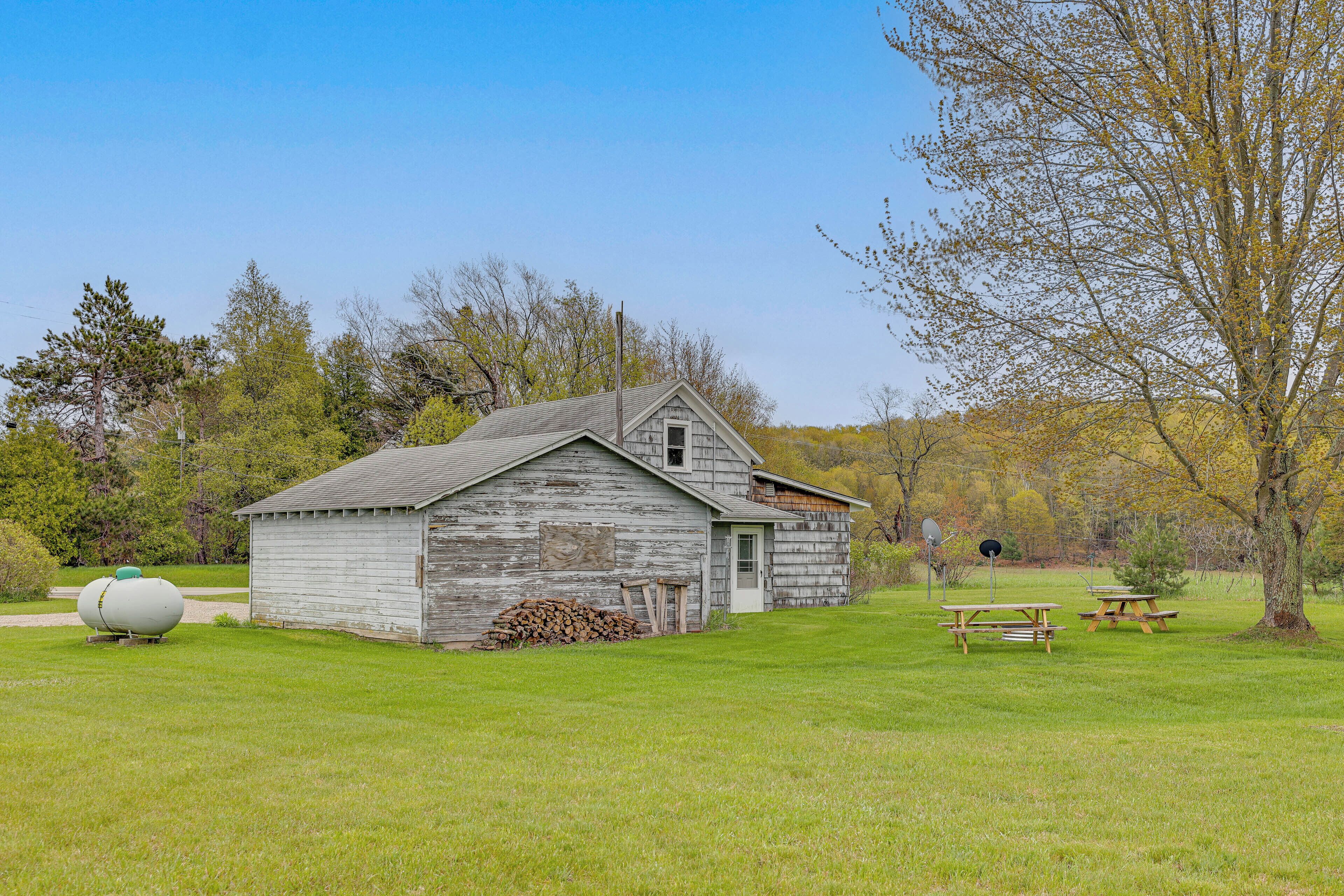 A rustic wooden building with a shed, picnic tables, and a large spherical object in a grassy field.