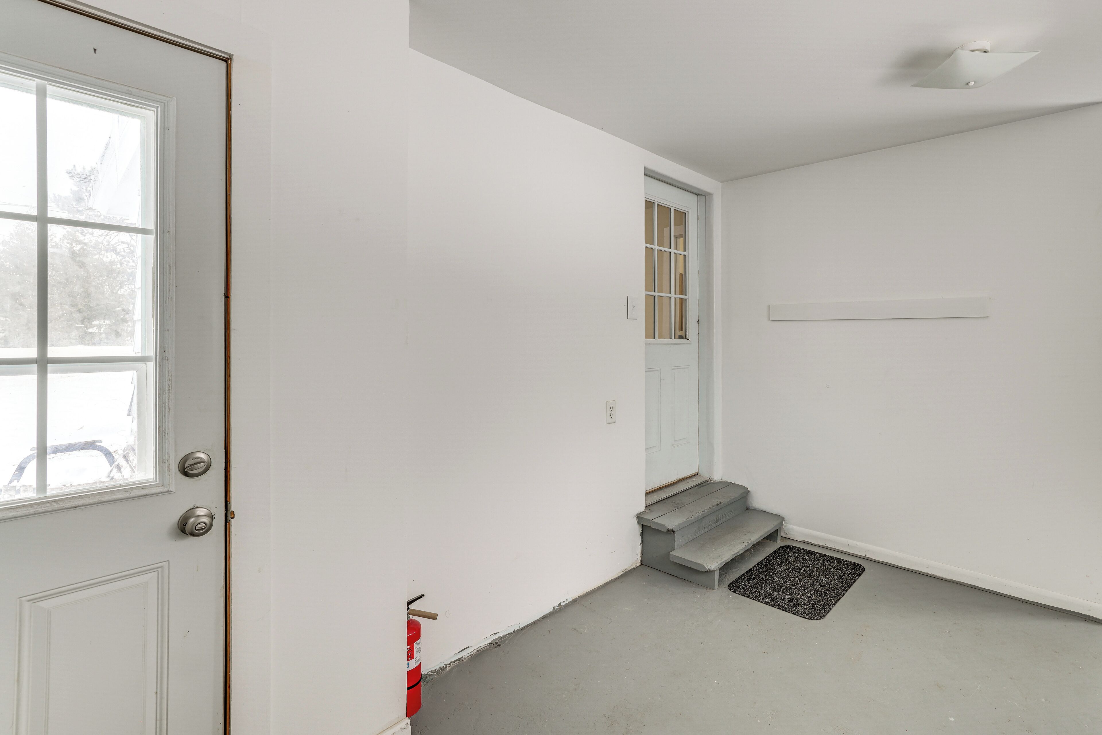 A clean, white interior with a door, a window, and a staircase leading to an upper floor.