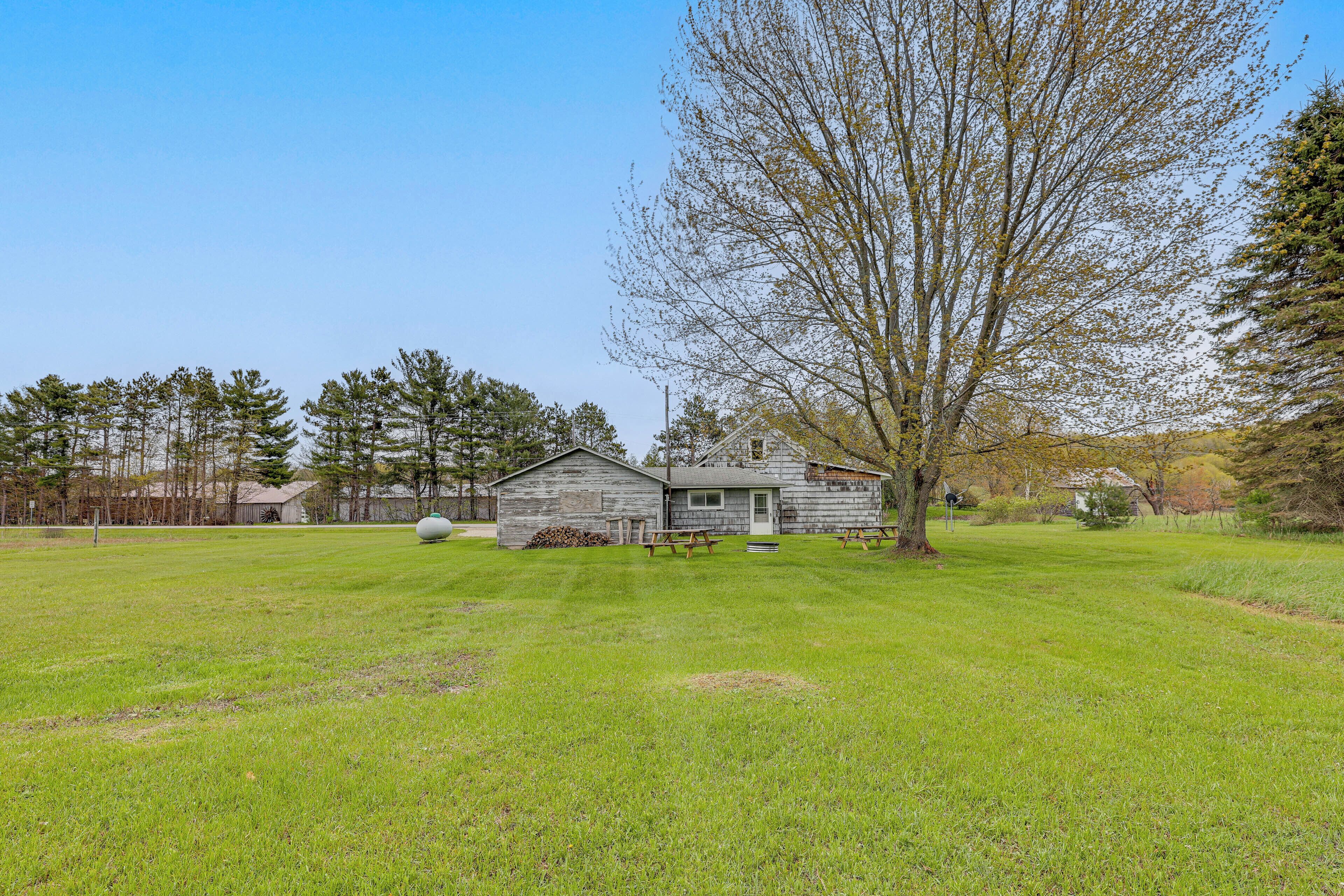 A rustic wooden cabin with a large lawn in front, surrounded by trees and a clear sky.