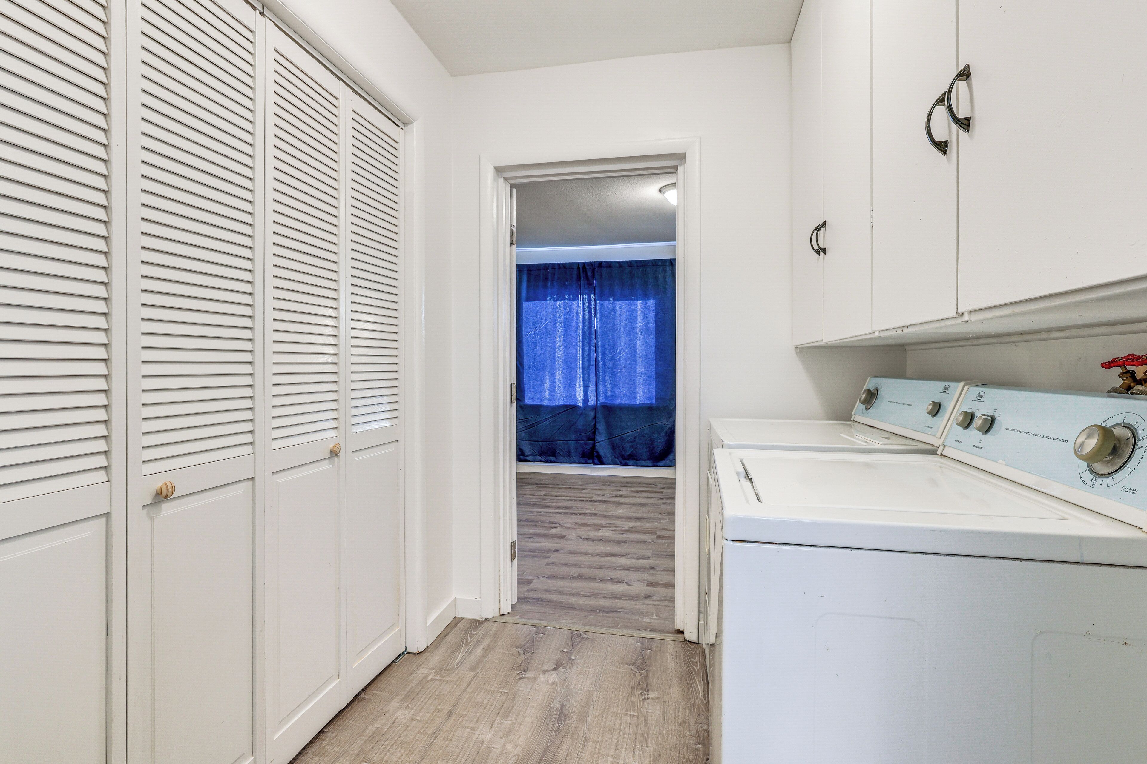 A laundry room with a washing machine, a dryer, and a white wardrobe with louvered doors.