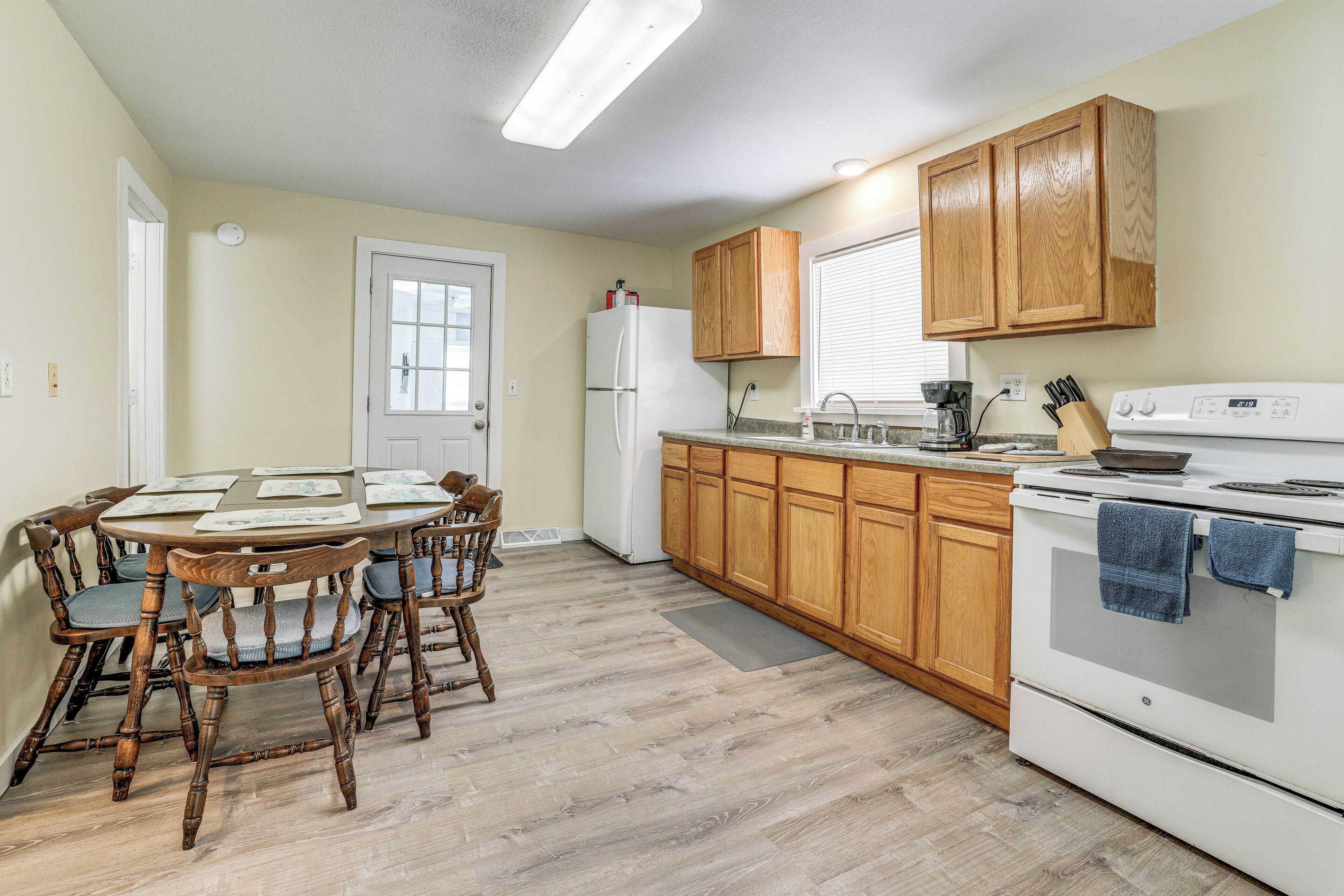 Une cuisine avec des meubles de rangement en bois, un réfrigérateur blanc, une cuisinière et une table à manger avec des chaises.
