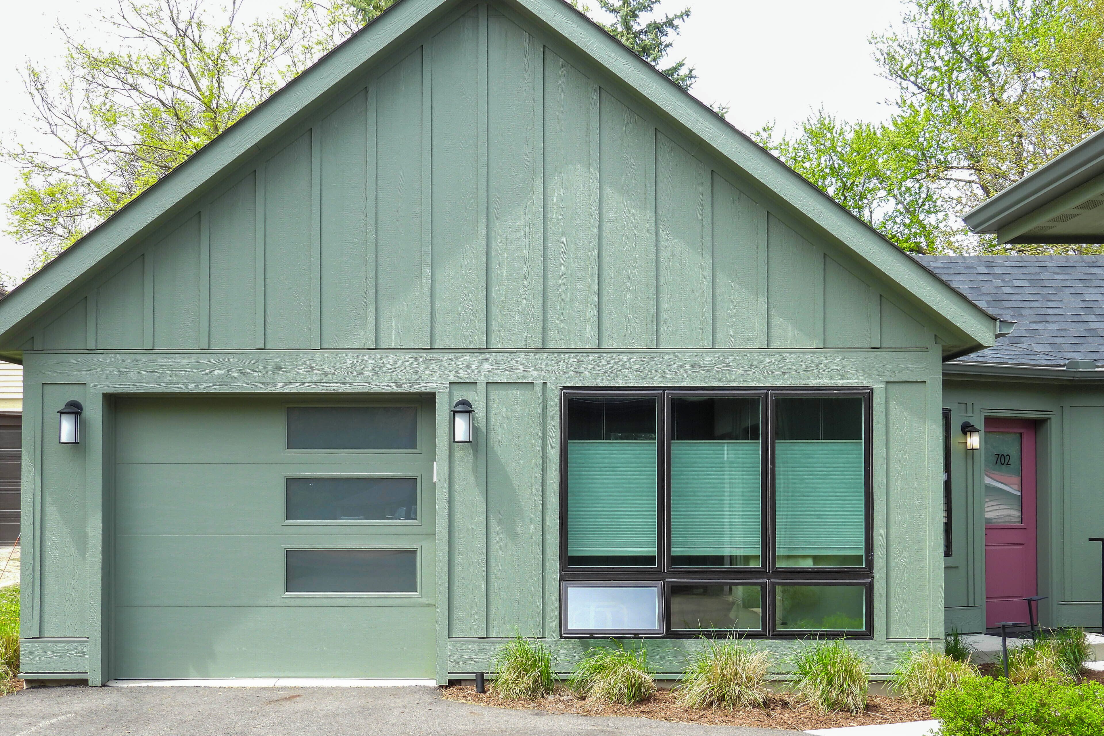 A green building with a garage door, three windows, and a door with the number 702.