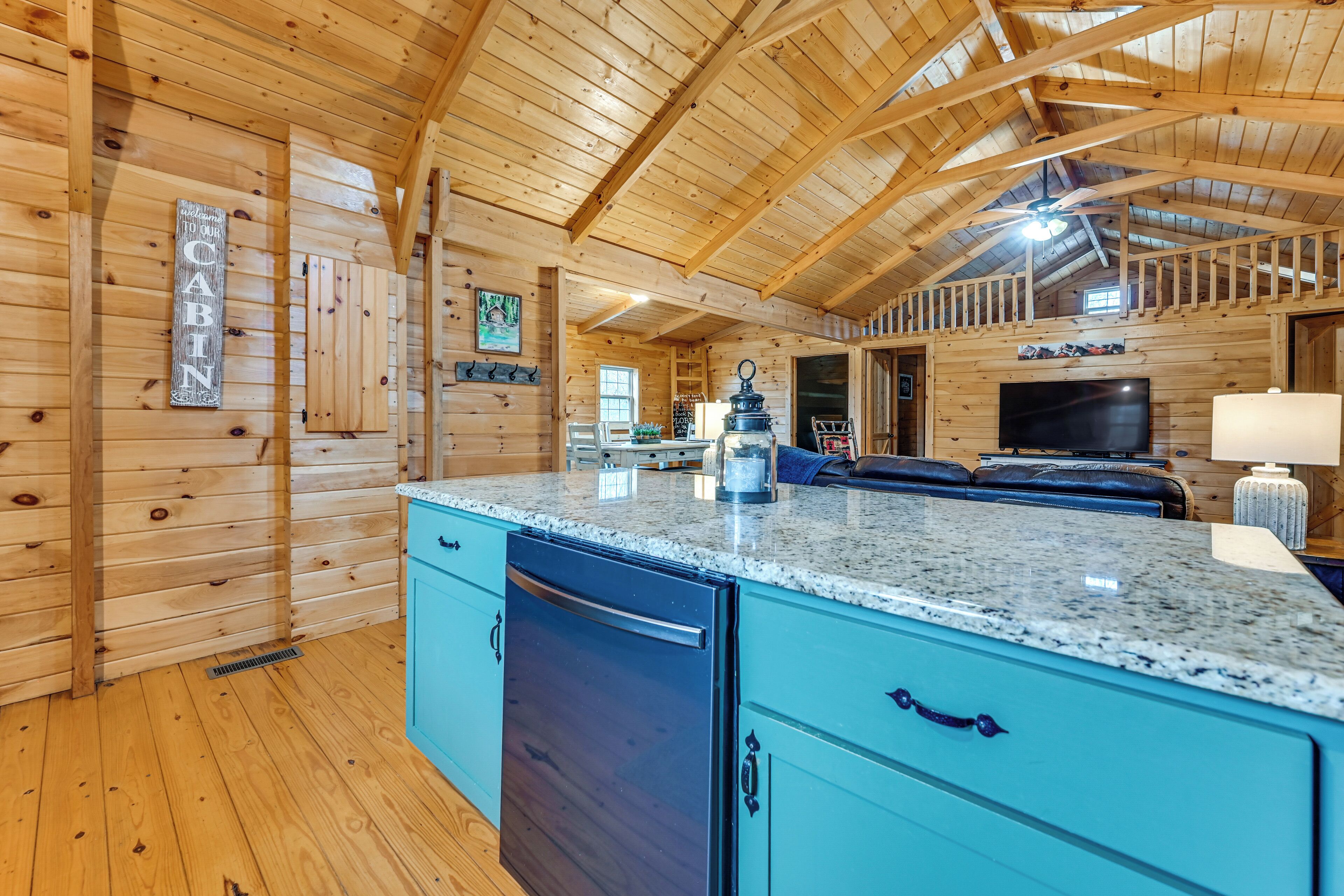 Una cabaña amplia con paredes de madera y un techo alto. Cuenta con una cocina y una encimera de granito, además de armarios azules.