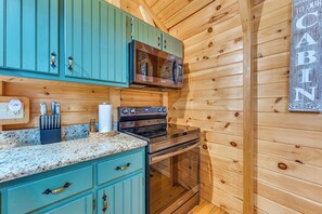 A kitchen with teal cabinets, a stainless steel stove, and a microwave. - Explore Mammoth Cave: Cabin w/ Fire Pit & Grill! (Cub Run)