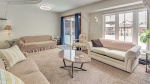 A living room with a sofa, armchair, and coffee table, a lamp, and a view through a large window. - Pet-friendly Siren Home! Walk to Bars & Lakes (Siren)