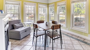 A dining area with a table and chairs, a gray sofa, and large windows with white frames. - Pool, Patio & Putting Green: Manchester Getaway (Manchester)