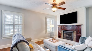 A living room with a fireplace, a ceiling fan, and a television mounted on the wall. - Pool, Patio & Putting Green: Manchester Getaway (Manchester)