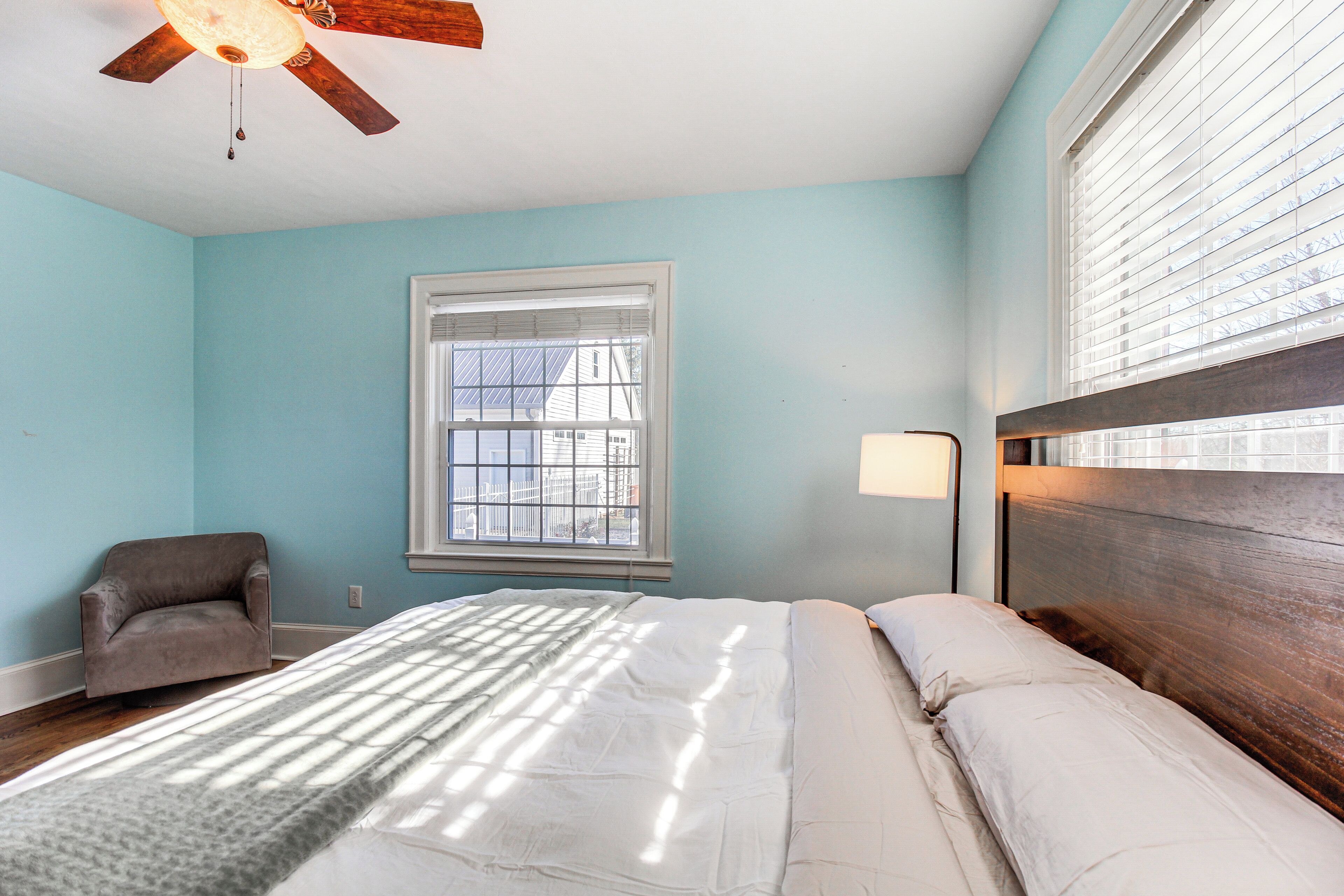 A bedroom with a bed, a chair, a window, and a ceiling fan.