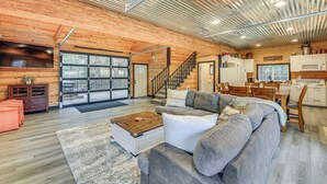 A spacious living area with a large gray sectional sofa, a wooden coffee table, and a kitchen area with white cabinets and a microwave. - Hot Tub & Fire Pit: Getaway on Pend Oreille River (Priest River)