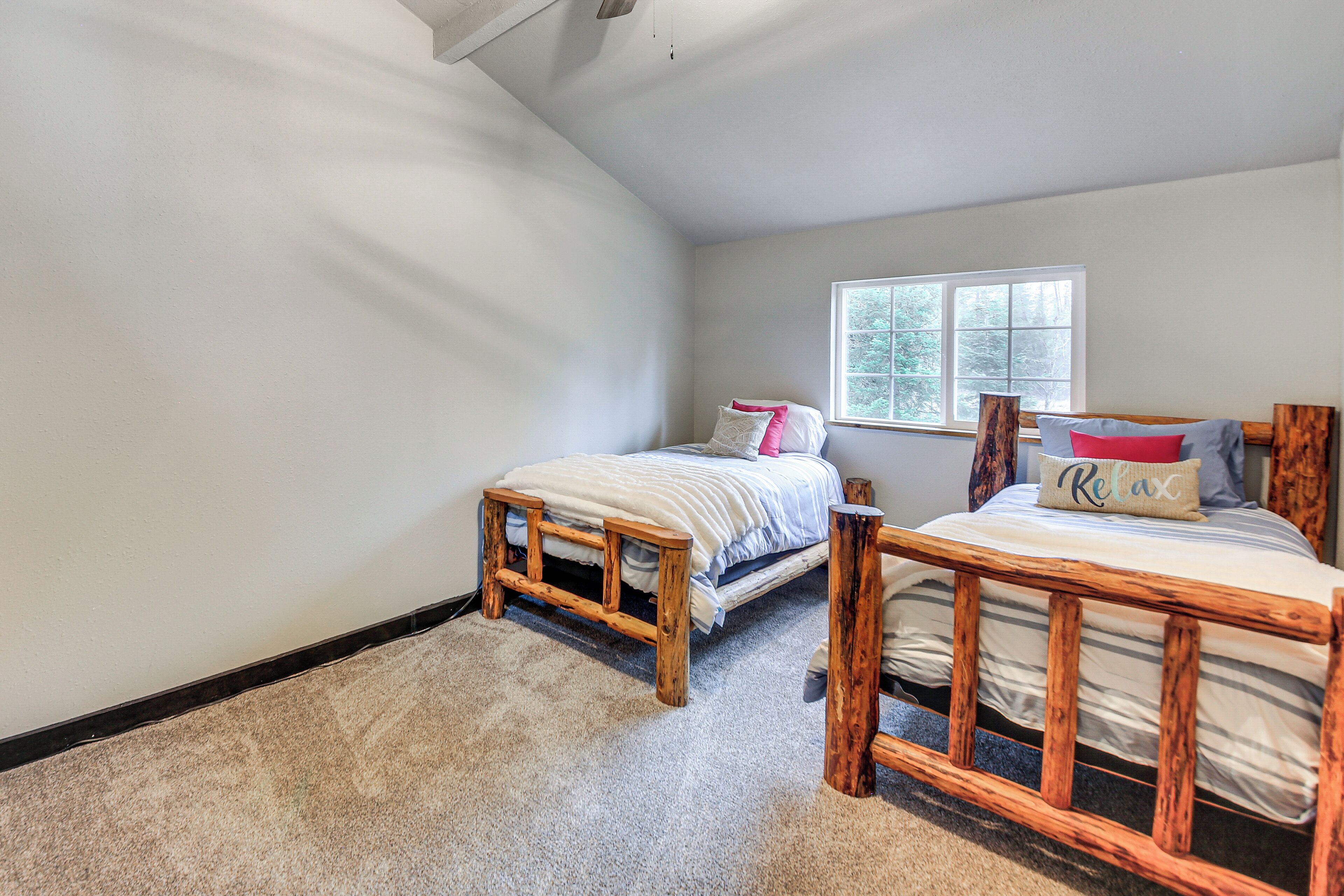 A bedroom with two wooden beds, a window with a view of trees, and a carpeted floor.