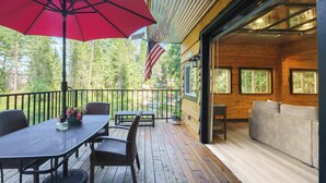 A wooden deck with a table and chairs, a red umbrella, and an American flag. - Hot Tub & Fire Pit: Getaway on Pend Oreille River (Priest River)