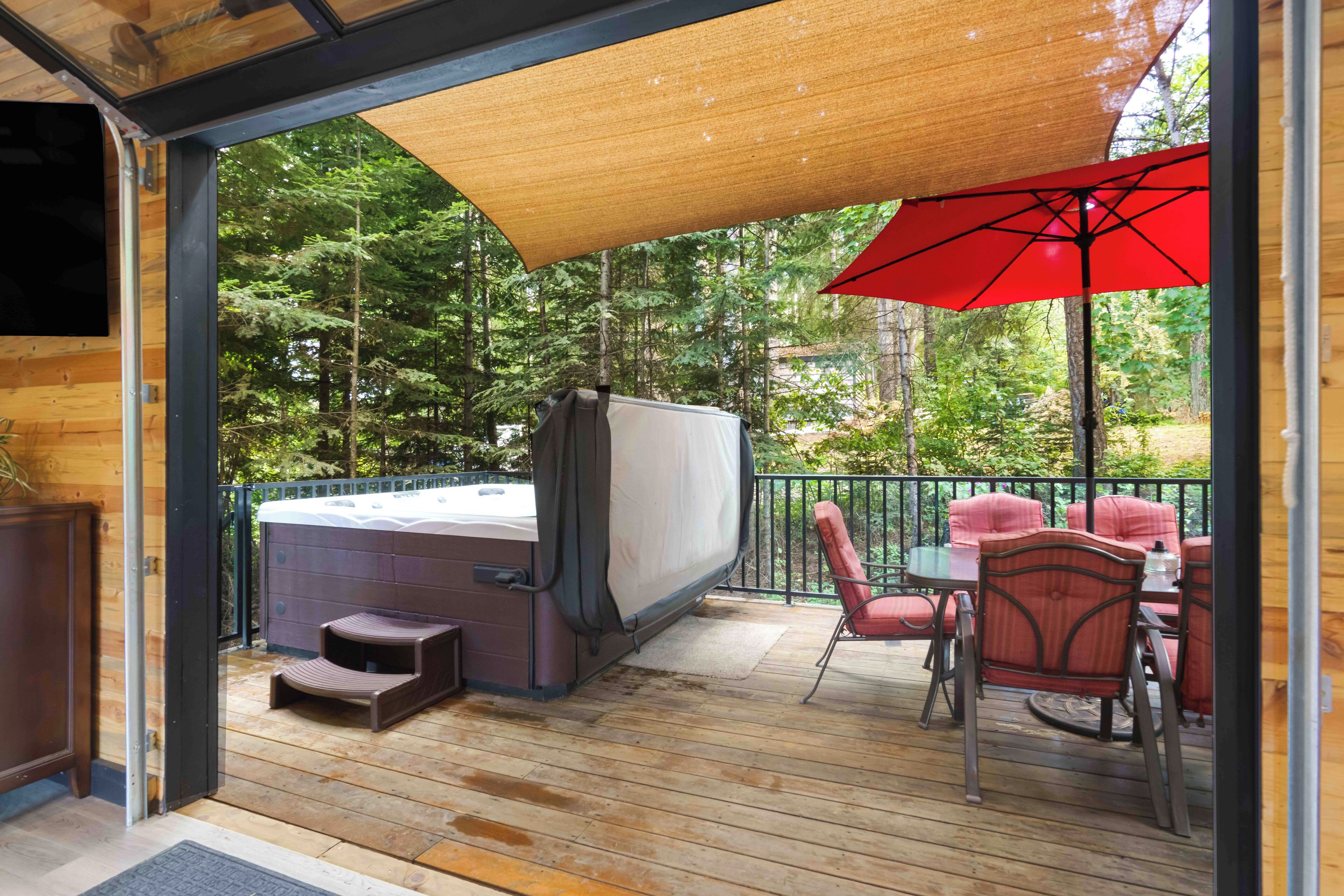 A wooden deck with a hot tub, red chairs, and a red umbrella.