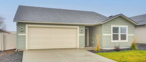 A single-story house with a garage, a front yard with grass and plants, and a concrete driveway.