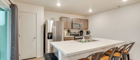 A modern kitchen with a central island, stainless steel appliances, and bar stools.