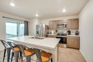 A modern kitchen with a central island, bar stools, wooden cabinets, stainless steel appliances, and a sliding glass door to the outside.