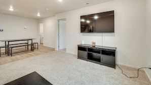 A spacious living area with a large flat-screen TV mounted on the wall, a dark wooden entertainment unit, and a light-colored carpet. - Walk to The Plains Golf Course: Getaway in Cheney! (Cheney)