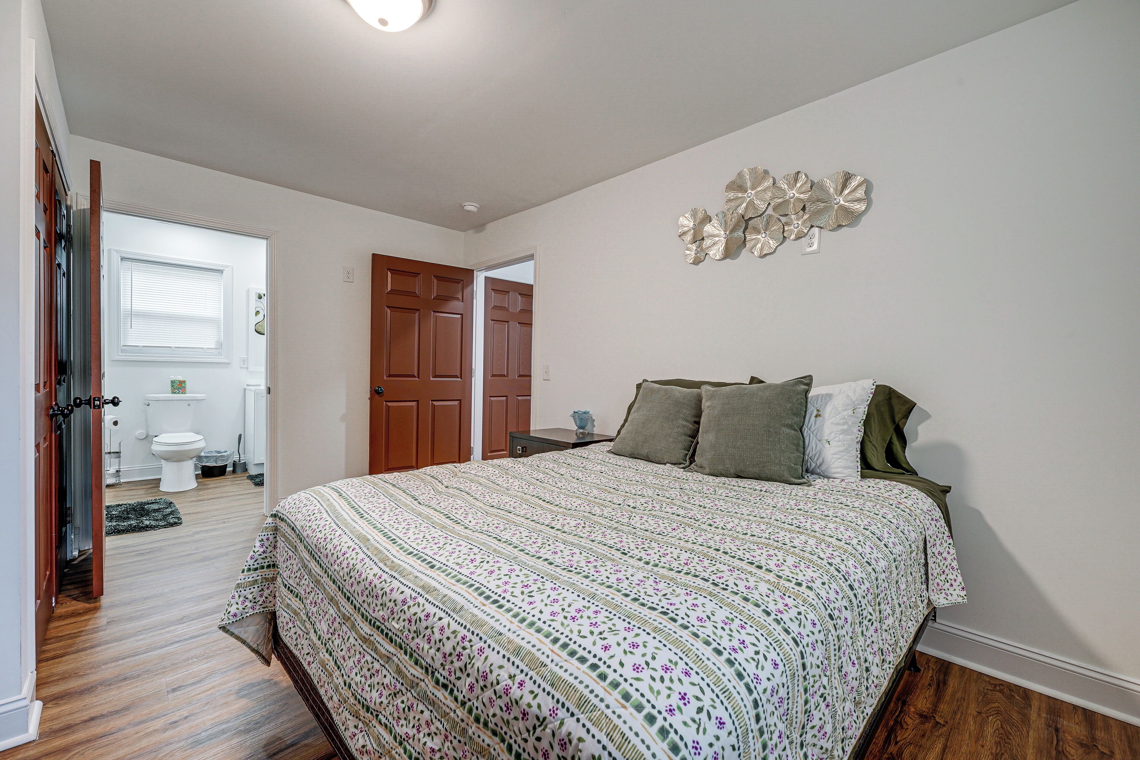Un dormitorio con una cama grande, piso de madera, una puerta que da al baño y un adorno en la pared.