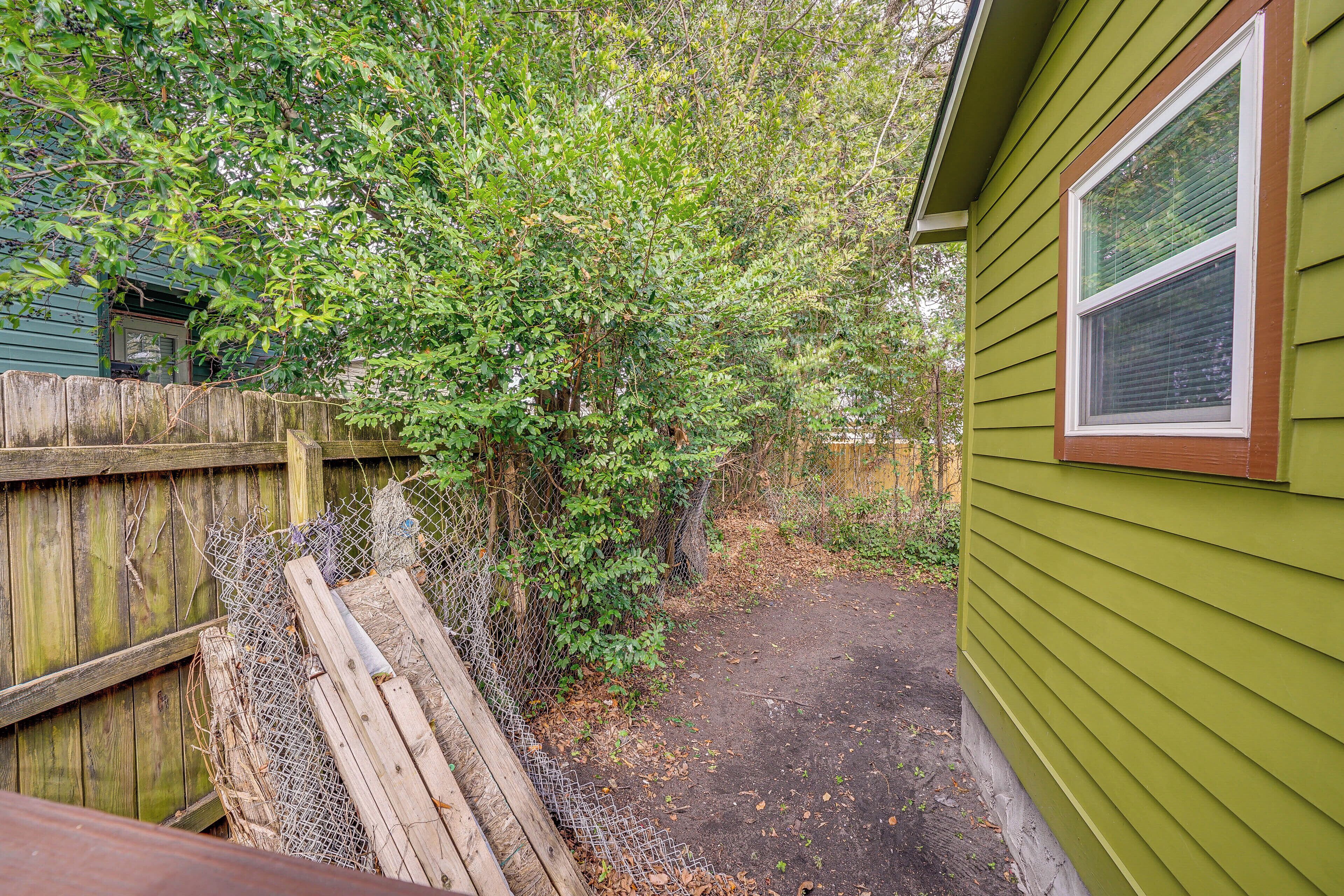 A fenced backyard with a wooden deck, a green house, and a dirt path.