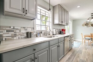 A modern kitchen with grey cabinets, a large window, and a dining area with a wooden table and chairs. - 1/2 Mi to River! Poolside Escape on Merritt Island (Merritt Island)