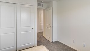 Een kamer met een vloerkleed, witte muren en een deur die naar een andere kamer leidt.