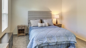 Een slaapkamer met een bed, nachtkastjes, een dressoir en een raam met jaloezieën.