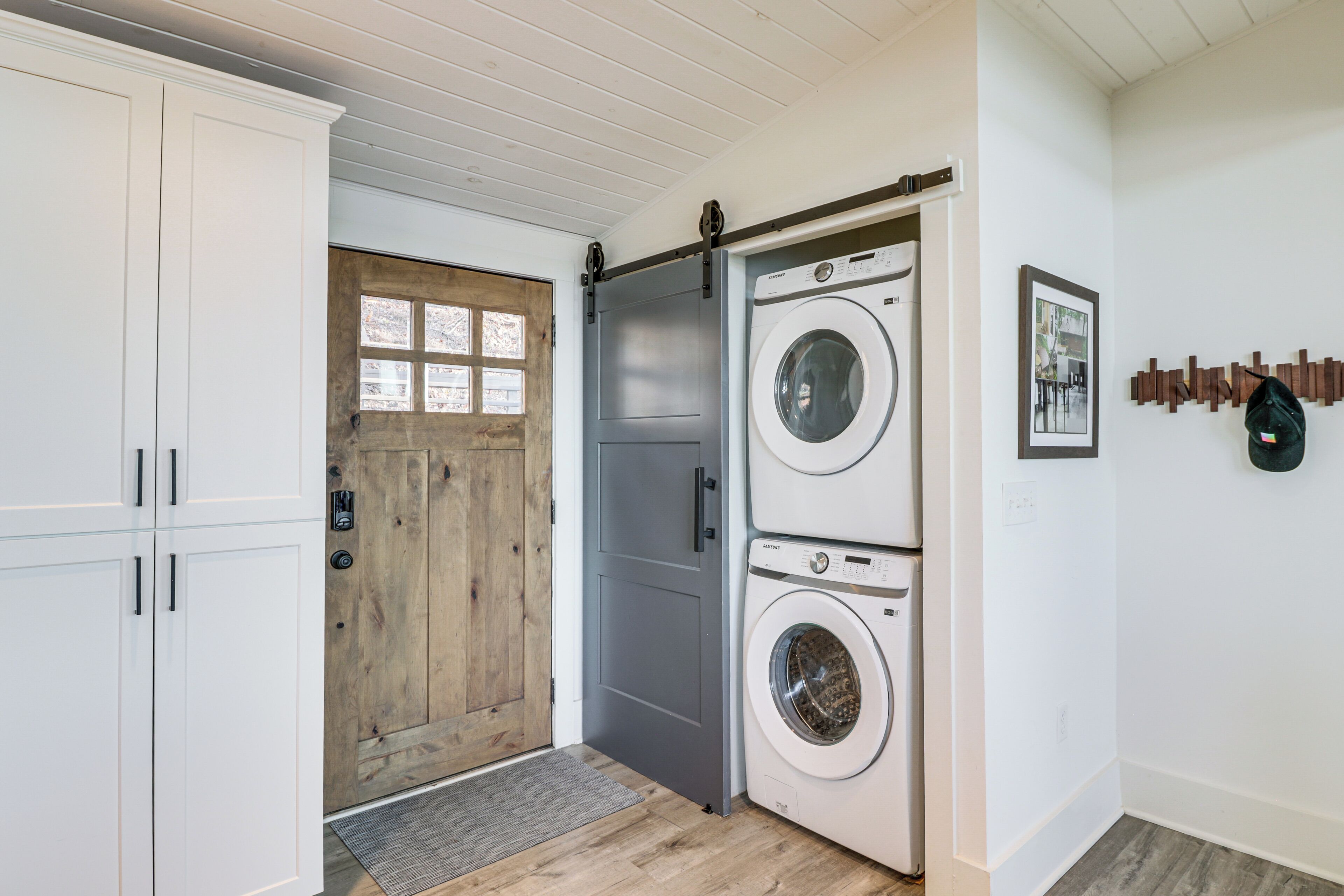 A laundry room with two stacked washing machines, a wooden door, and a white wall with a framed picture.