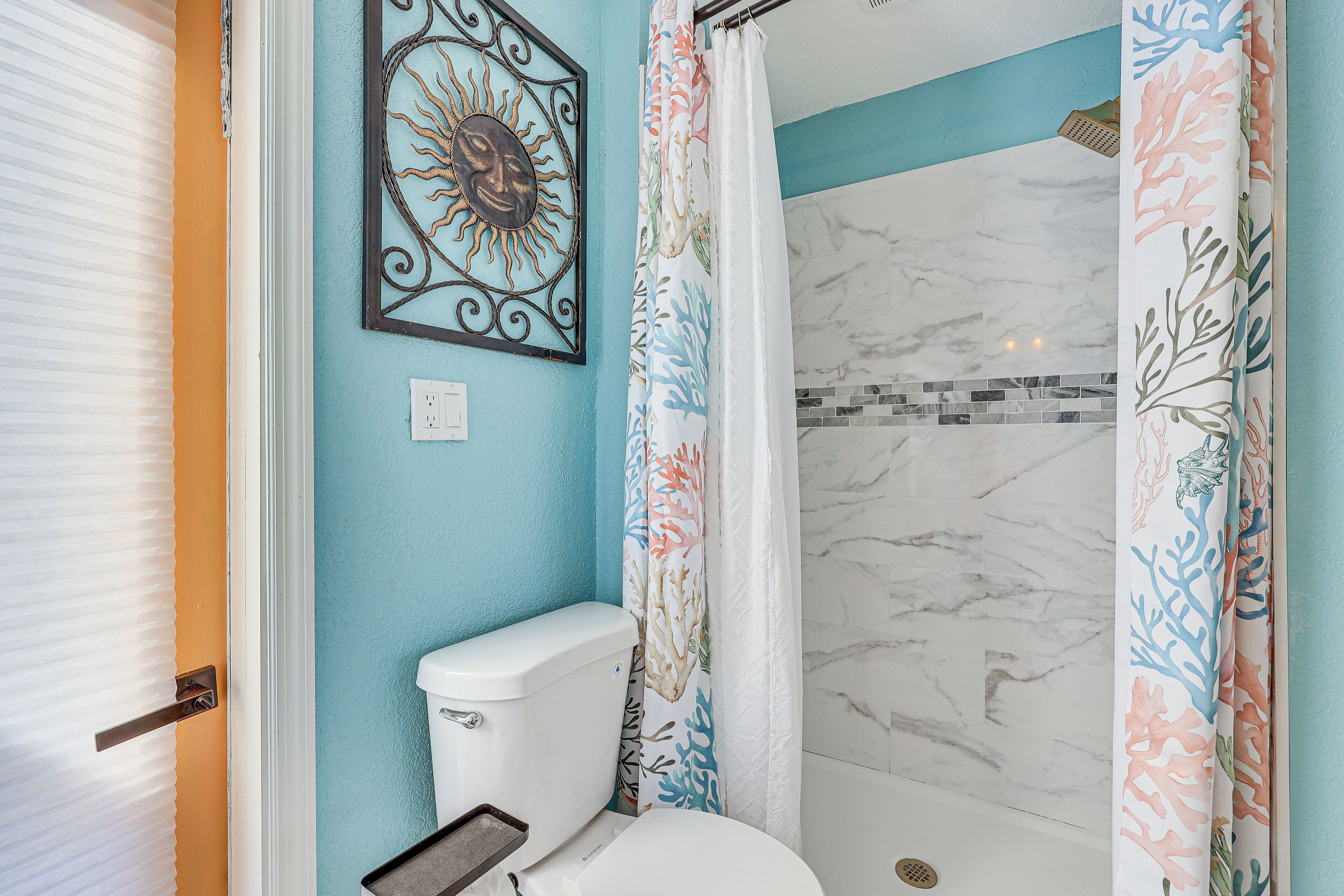 A bathroom with a toilet, a shower with a coral-patterned curtain, and a wall with a sun design.