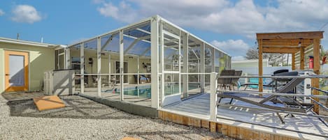 Una estructura con paredes de vidrio que incluye una piscina, terraza de madera y zona de estar al aire libre.