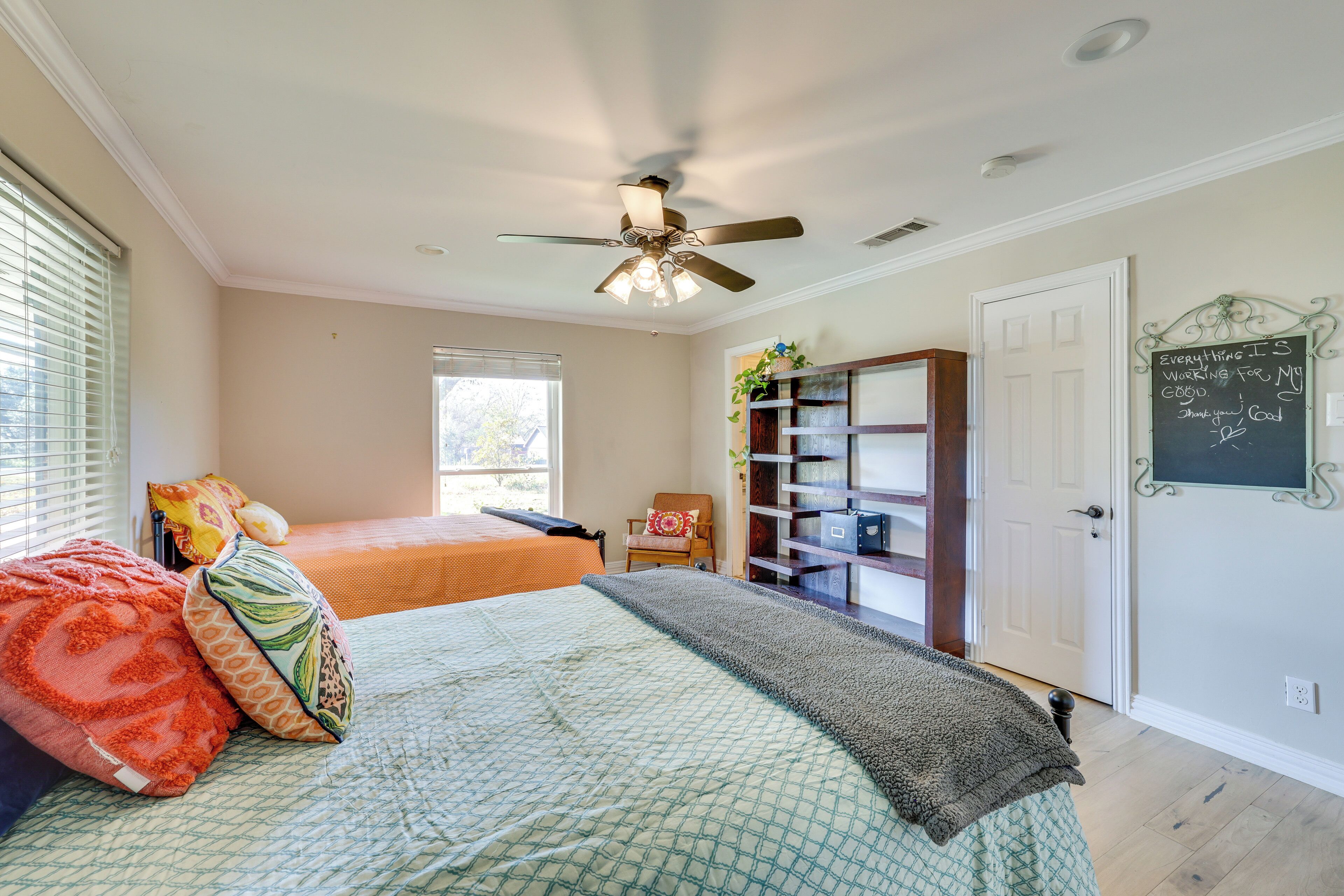 A bedroom with two beds, a ceiling fan, a bookshelf, and a chalkboard with a message.