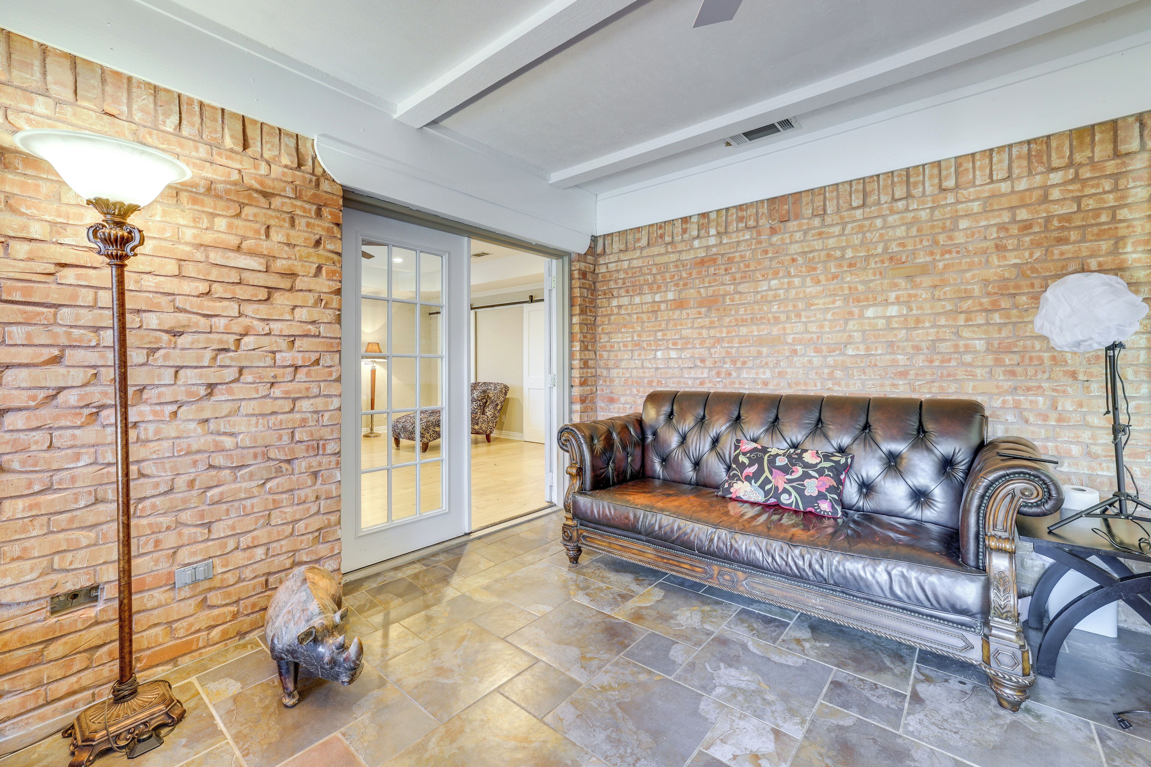 A room with a brick wall, a leather sofa, a floor lamp, and a decorative pig statue.