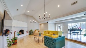 Uma sala de estar ampla com lareira, um sofá amarelo, uma poltrona azul-turquesa e um piano de cauda ao fundo.
