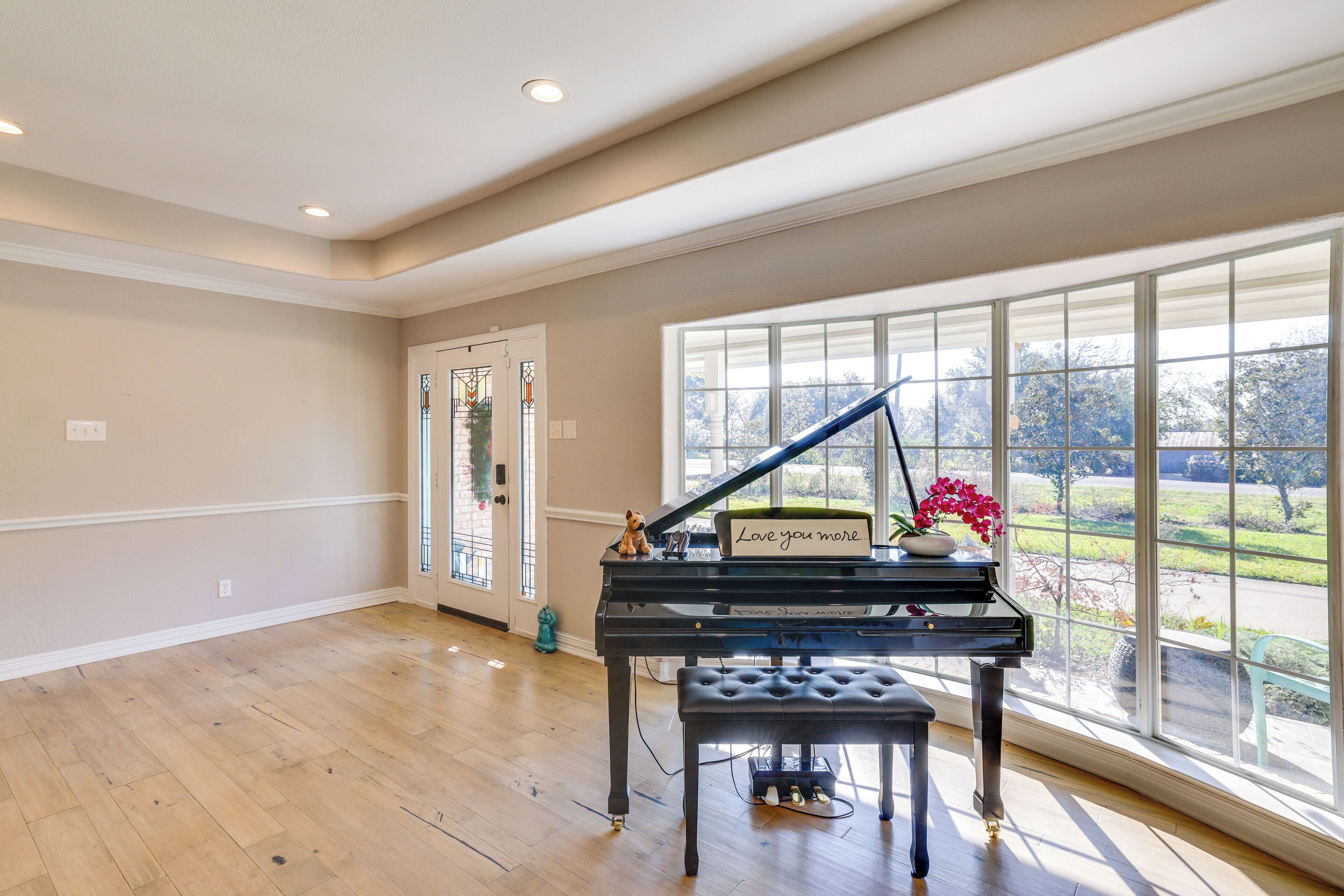A grand piano in a spacious room with large windows offering a view of a landscaped area.