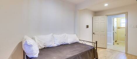 A bedroom with a bed, white walls, and a wooden floor.