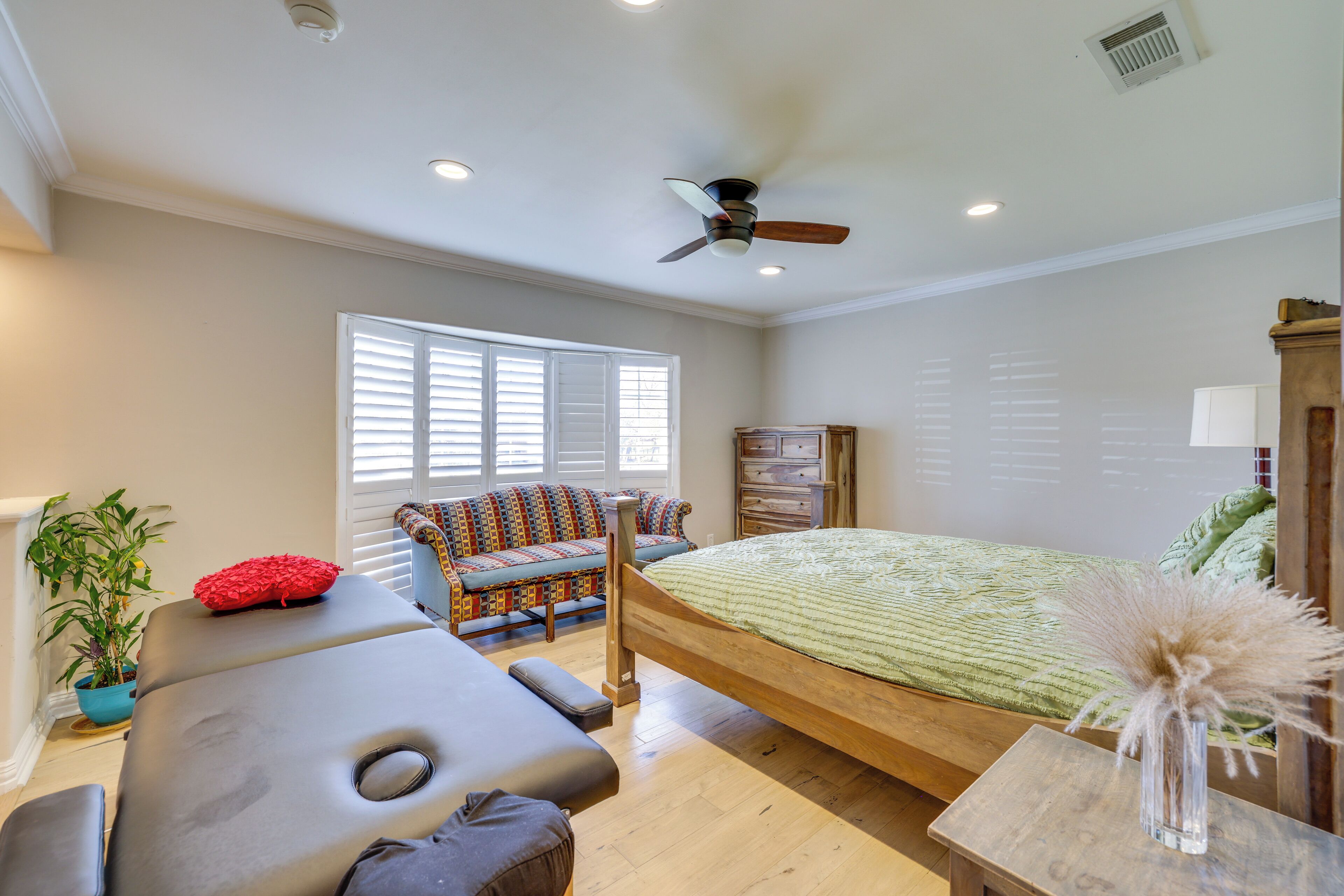 A bedroom with a bed, a sofa, a massage table, and a ceiling fan.