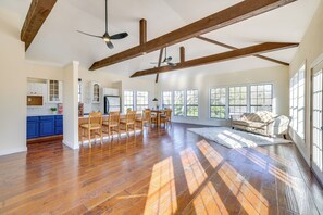 Uma sala de estar ampla com piso de madeira, um conjunto de jantar e grandes janelas que oferecem muita luz natural.