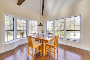 A dining room with a wooden table and chairs, large windows, and a pendant light.