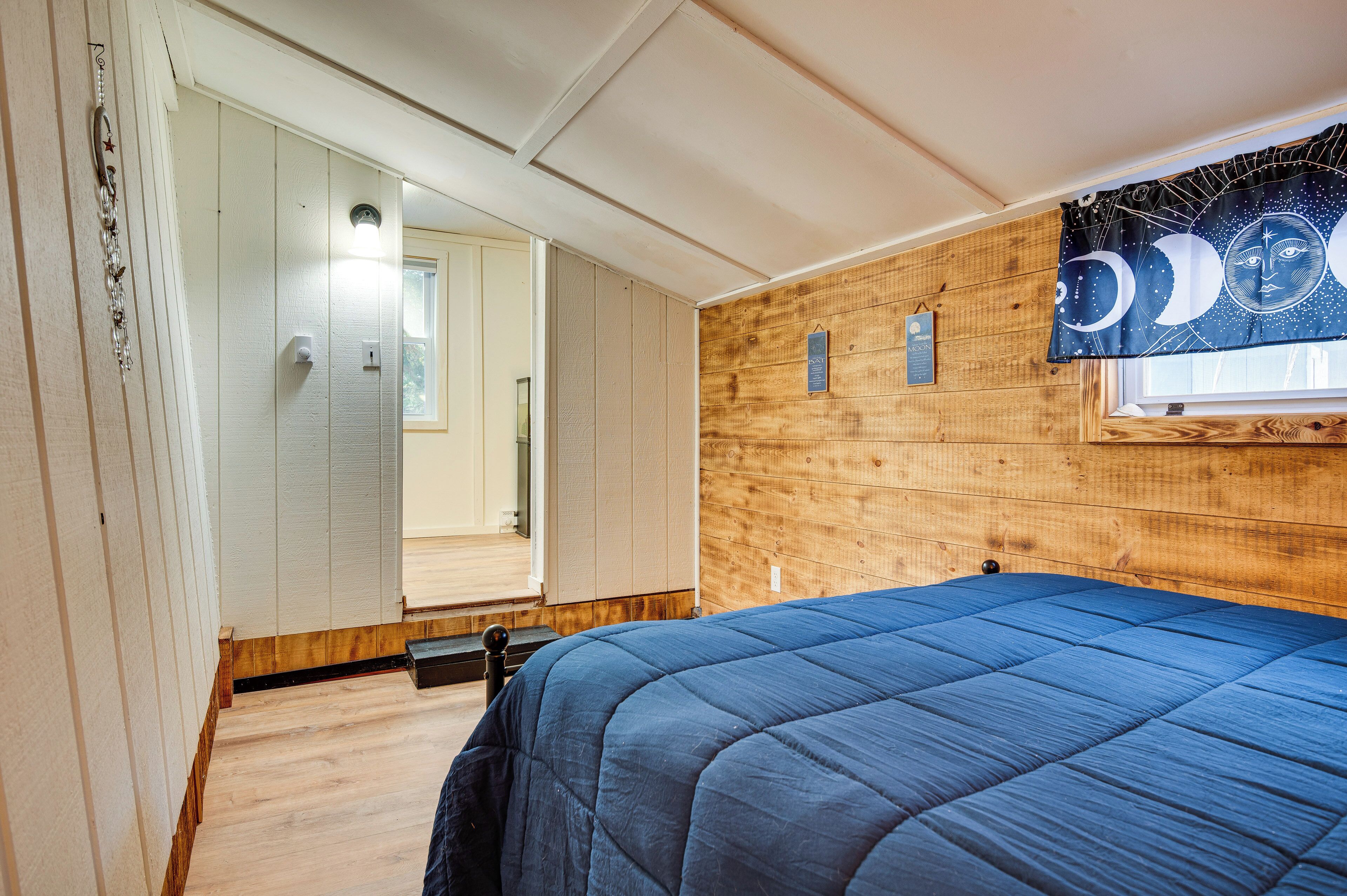 Ein Schlafzimmer mit Holzwand, einem Bett mit blauer Bettdecke und einem Fenster mit Vorhang.