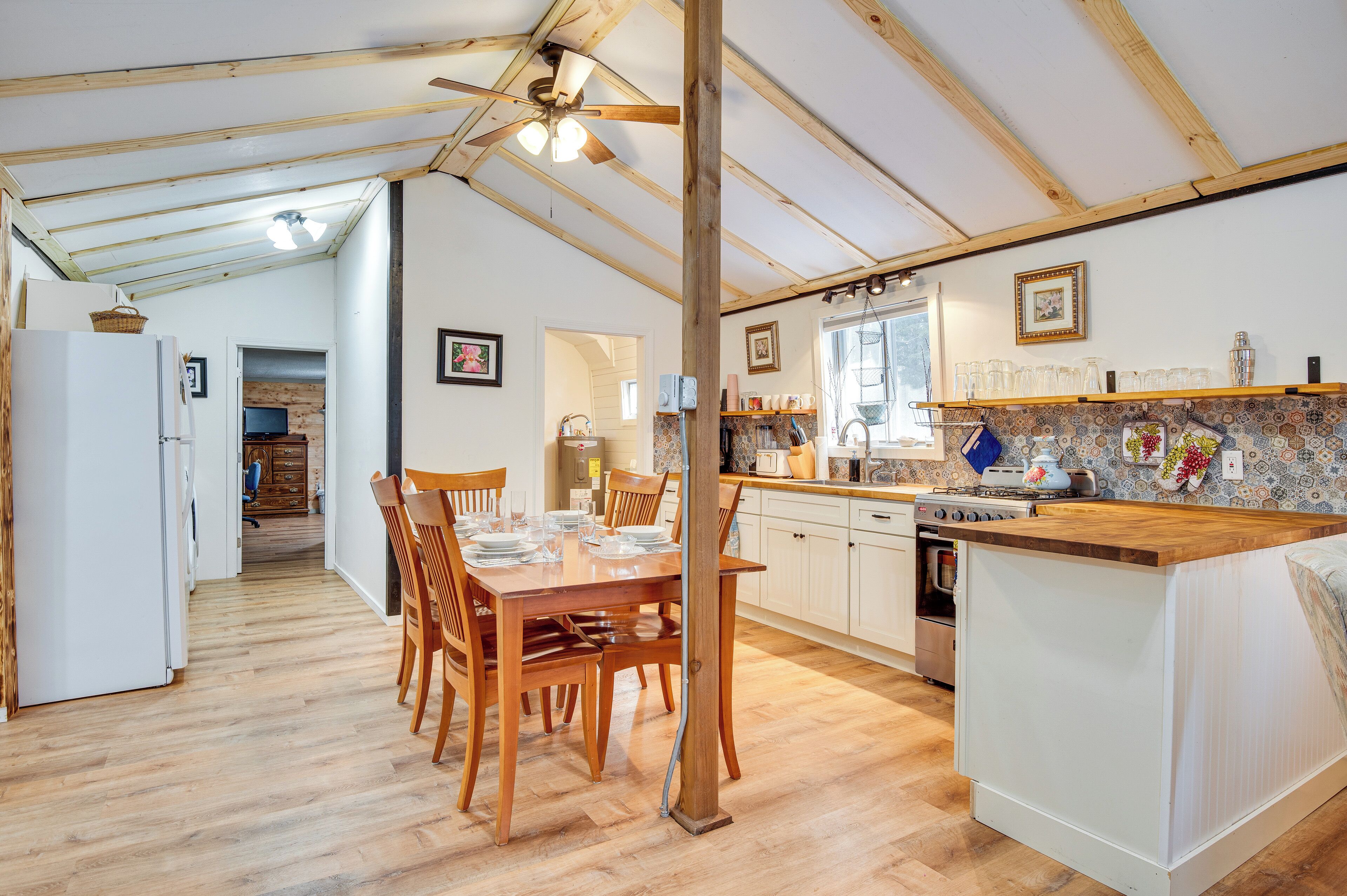 A kitchen with wooden cabinets, a wooden dining table with chairs, a built-in island with a sink, and a ceiling fan.