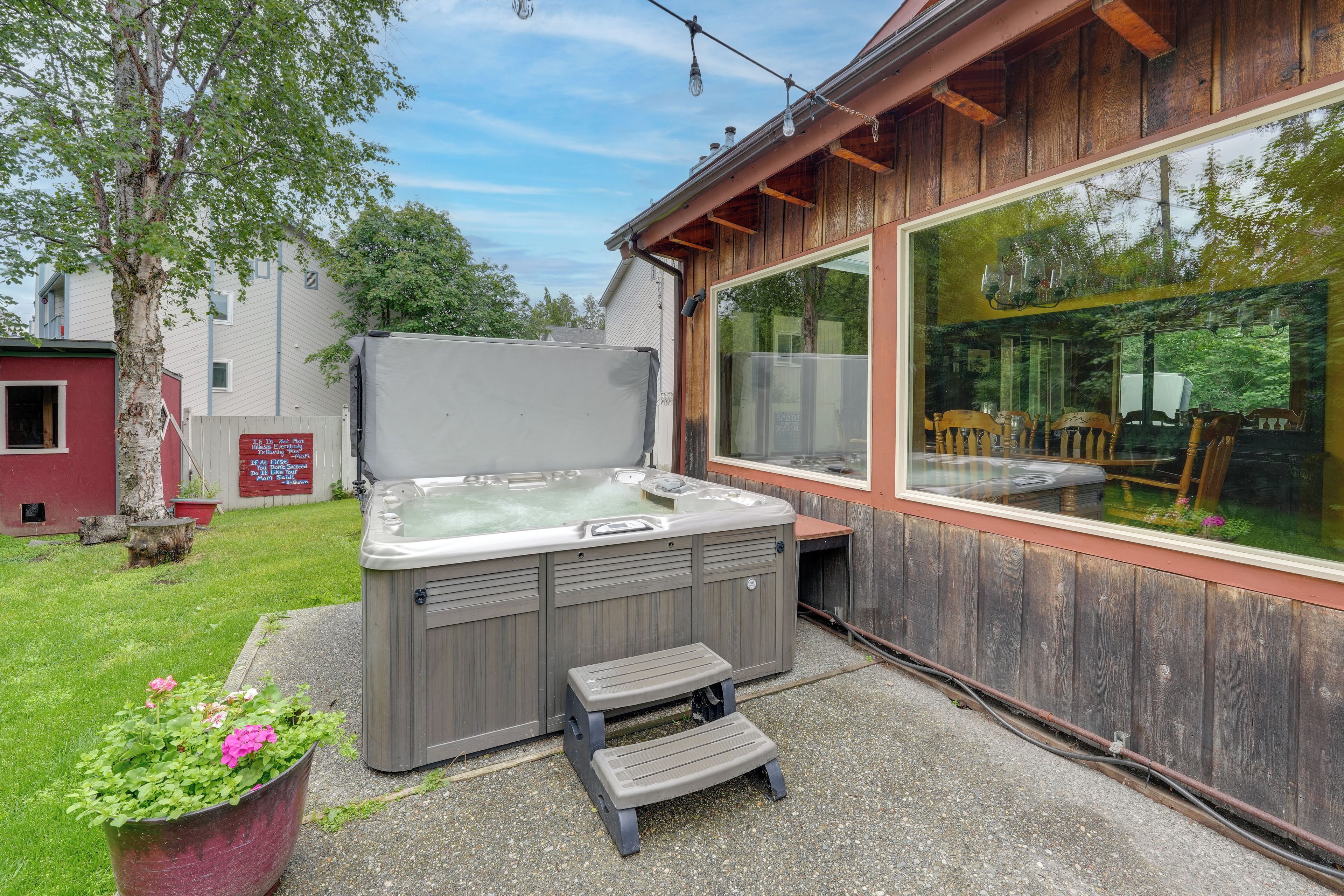 A hot tub with a wooden deck, a large window, and a step leading to it.
